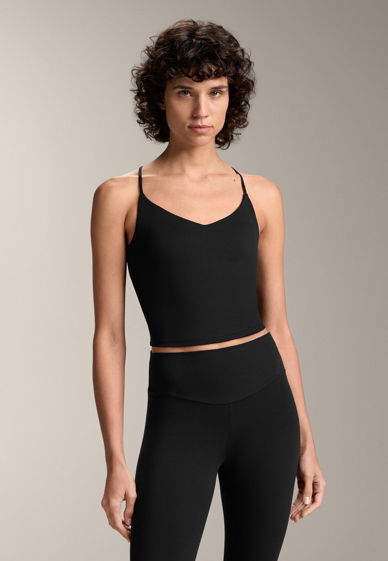 Fekete, rövidített tank top vékony pántokkal és V nyakkivágással, sima anyagból készült. Magas derekú leggings-szel párosítva.