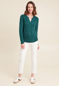 Maglione lavorato a maglia in teal con scollo a V, dettaglio dei bottoni e motivo testurizzato. Abbinato a pantaloni bianchi slim-fit e sneakers casual.
