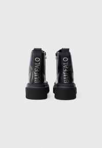 Botas de cuero negro hasta el tobillo con suela gruesa, con una lengüeta en la parte trasera y el logotipo plateado "BUFFALO" en la parte posterior. Textura suave.