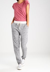 Grå marl sweatpants med elastisk midjeband och dragsnodd, parat med en kortärmad rosa topp. Modellen står med händerna i fickorna.