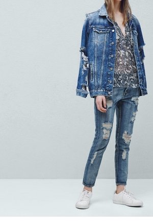 Giacca di jeans con maniche usurate, blusa a fantasia, jeans skinny strappati e sneakers bianche. Tutti gli articoli in varie tonalità di blu.