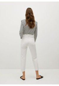 Jeans blancos de cintura alta y dobladillo recortado, combinados con una camisa de rayas en blanco y negro de manga larga. El calzado son sandalias negras.
