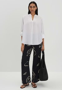 White, long-sleeve, collared blouse paired with black wide-leg pants featuring abstract off-white patterns, carrying a textured black bag.