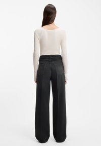 Beżowa bluzka z długim rękawem i szerokim dekoltem, zestawiona z luźnymi, czarnymi spodniami dżinsowymi z wysokim stanem, posiadającymi tylne kieszenie i ozdobne przeszycia.