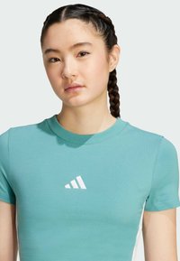Turkos kortärmad t-shirt i mjukt tyg, med en vit Adidas-logotyp på framsidan och en klassisk rund halsringning.