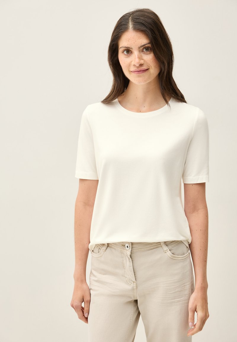 Witte T-shirt met korte mouwen, een ronde halslijn en zachte stof, gecombineerd met lichtbeige broeken met een knoop aan de voorkant en een zakdetail.