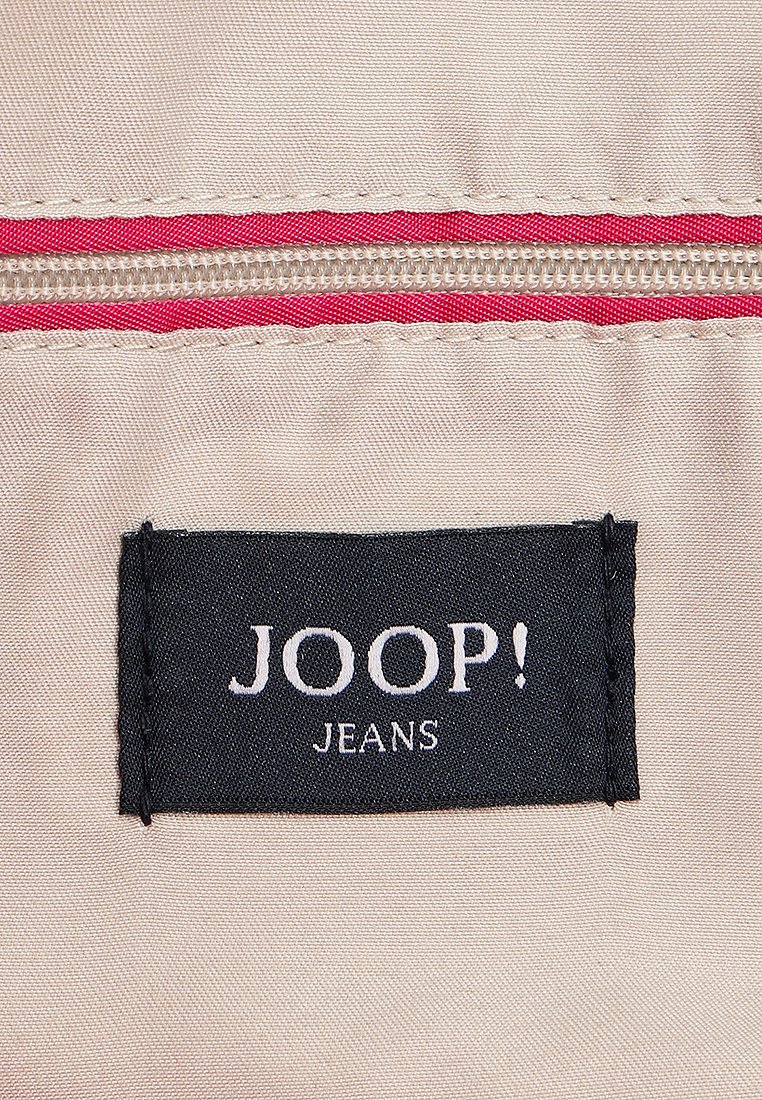 Beige Stoff mit einem roten Reißverschlussdetail. Ein schwarzes Etikett mit der Aufschrift "JOOP! JEANS" in weißem Text ist auffällig auf dem Stoff platziert.