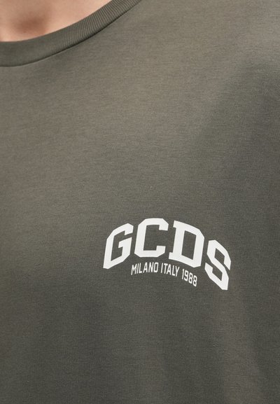 Olivno zeleni bombažni T-shirt s krožnim ovratnikom in belim natisnjenim besedilom: "GCDS MILANO ITALIJA 1988" v ukrivljenem dizajnu na prsih.