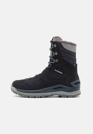 Dark blue winter boot with suede and textile material, grey fleece collar, blue laces, and textured rubber sole. Features metal eyelets.