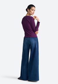 Purple ribbed long-sleeve top paired with wide-leg blue jeans, featuring a rounded neckline and back design detail. Smooth texture.