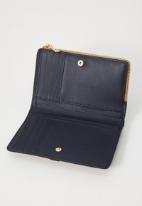 Intérieur d'un portefeuille en cuir marine avec plusieurs emplacements pour cartes, une fermeture à bouton-pression et un compartiment zippé. Des accents en matériel doré sont présents.