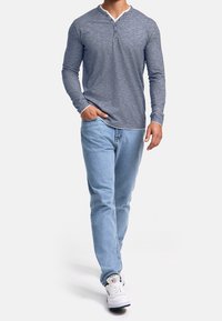 Long-sleeve gray henley shirt with a textured design and a white collar, paired with light blue jeans and white sneakers.