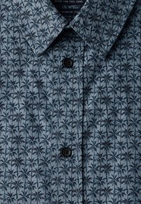 Blue button-up shirt with dark palm tree pattern and regular fit label visible inside the collar.