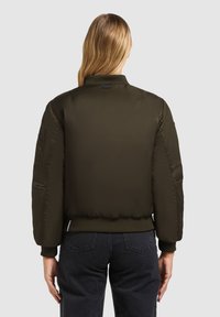 Olivovo zelená bomber bunda s prešívaným dizajnom, rebrovanými manžetami a vysokým golierom. Obsahuje bočné vrecká a elegantný vzhľad. Zobrazený zadný pohľad.
