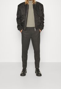 Giacca bomber nera con una texture liscia, dolcevita grigio e pantaloni tapered grigio scuro. Stivali neri stringati completano l'outfit.