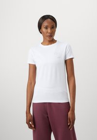 T-shirt bianco a maniche corte realizzato in tessuto liscio, con un sottile design ricamato grigio nell'area sinistra del petto.