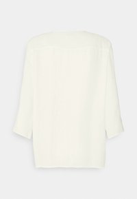 Blusa blanca texturizada de corte holgado, con mangas tres cuartos y escote redondeado. La parte trasera muestra detalles simples de costura.