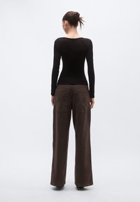 Μαύρο εφαρμοστό τοπ με μακριά μανίκια, σε συνδυασμό με σκούρο καφέ παντελόνι με φαρδιά πόδια, πίσω τσέπες και υφασμάτινη υφή με λεία επιφάνεια.