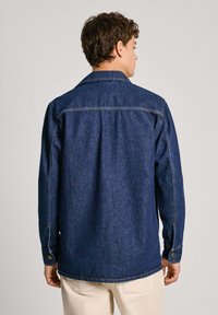 Camicia in denim scuro con colletto a punta, maniche lunghe e polsini con bottoni. Presenta una vestibilità comoda e dettagli di cucitura sottili.