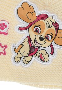 Knitted yellow cap featuring an embroidered cartoon dog with brown and tan fur, wearing a pink outfit and hat, with decorative pink accents.