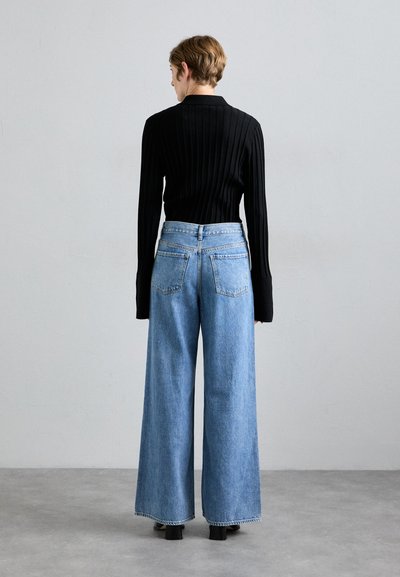 Schwarzes Ripp-Langarmoberteil kombiniert mit weit geschnittenen hellblauen Jeans. Die Jeans haben einen hohen Bund und zwei Gesäßtaschen.