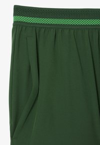Pantalones deportivos verdes con una cinturilla texturizada en verde, que cuentan con bolsillos laterales y una tela suave y ligera.