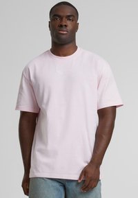 Pink cotton t-shirt with short sleeves, featuring a round neckline and a subtle embroidered logo on the chest. Smooth texture.