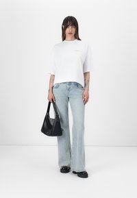 Bílý oversize tričko s krátkými rukávy, světle modré zvonové džíny, černá kabelka a masivní černé boty. Minimalistický design s jemným brandováním.