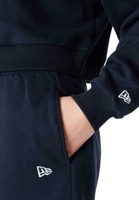 Felpa navy con polsini e vita a costine, caratterizzata da un logo ricamato sulla manica. Include una tasca laterale e una texture morbida.