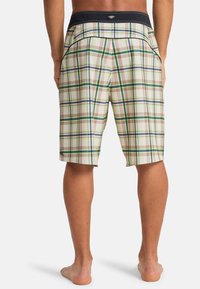 Μαγιό βερμούδα καρό σε μπεζ με πράσινες, μπλε και καφέ γραμμές· διαθέτει μαύρη ελαστική μέση και πλαϊνές τσέπες.
