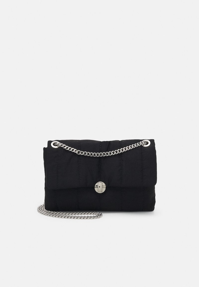 Zwarte doorgestikte crossbodytas met zilveren kettingriem en cirkelvormige metalen sluiting op het voorflapje.