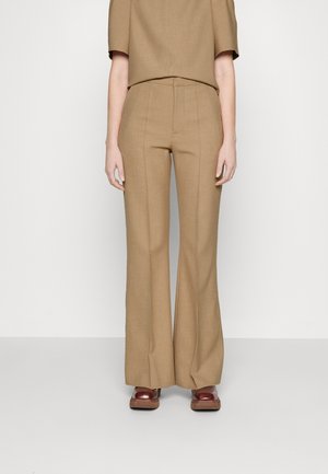 Kõrge vöökohaga, flared jalgadega püksid heledast pruuni kangast, mis on siledat tekstuuri, esifrooni õmblustega ja pressitud sobivusega.