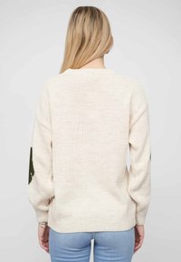 Cream-colored knit sweater with a loose fit, featuring dark green accents on sleeves and ribbed cuffs. Soft texture and crew neckline.