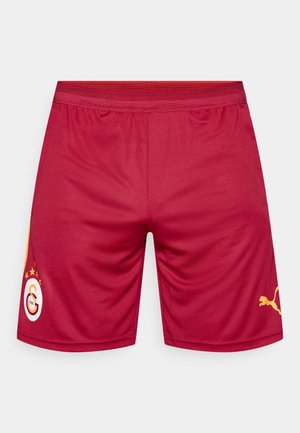 Pantalones cortos deportivos rojos con una cintura elástica, que presentan un logo amarillo y un acento, y una textura de tela suave. Sin patrones visibles.