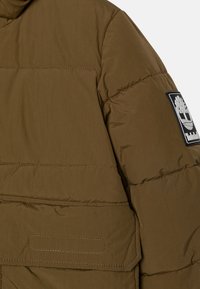 Ελαιόχρωμο μπουφάν με απαλή υφή, διαθέτοντας λογότυπο με μπα patch στο μανίκι και μπροστινή τσέπη με ραμμένες λεπτομέρειες.