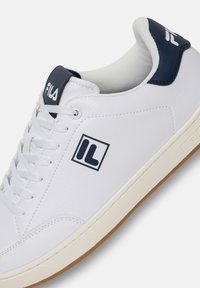 Białe skórzane sneakersy z niebieskimi akcentami i teksturowanym językiem. Posiadają gumową podeszwę oraz wyraźne logo blisko sznurówek i na pięcie.