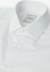 Weißes Hemd mit kragen und glatter Oberfläche, versehen mit einem Etikett "NEXT TAILORING" und zwei Knopfverschlüssen auf der Vorderseite.