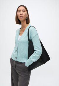 Ανοιχτό μπλε καρντιγκάν με V-νεκ, κλείσιμο με κουμπιά και ριμπ μήκος, συνδυασμένο με μαύρη τσάντα ώμου και γκρι παντελόνι. Λείος υφασματικός ιστός, άνετος σχεδιασμός.