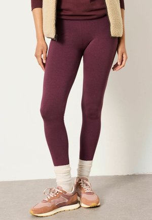 Person wearing maroon leggings, cream scrunched socks, pink and beige sneakers, and a beige fleece vest with maroon top.