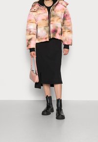 Giacca imbottita con un motivo degradé rosa e beige, dotata di chiusura con zip e cappuccio. Gonna nera, borsa rosa e stivaletti neri.
