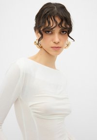 Långärmad vit topp gjord av lätt material, med sammetsdetaljer fram och en vid halsringning.