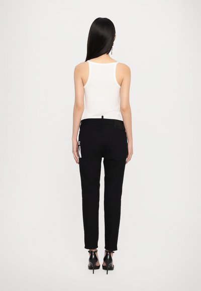 Zwarte denim jeans met een slim fit, voorzien van een opgestikte zak met witte tekst en een gestructureerde tailleband, gecombineerd met een witte tanktop.