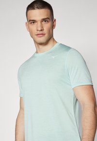 Camiseta atlética de color azul claro con mangas cortas, hecha de una tela suave y texturizada. Presenta un pequeño logotipo blanco en la parte superior del lado izquierdo del pecho.
