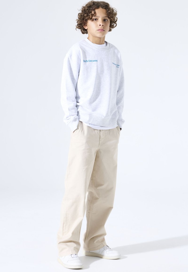 Sudadera gris con texto "Tech Dreams", pantalones beige de corte ancho y zapatillas blancas, mostrados sobre un fondo claro y liso.