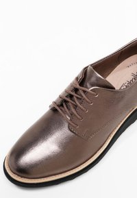 Bruine metalen veterschoen met een gladde textuur, afgeronde neus en contrasterende zwarte zool; minimalistisch ontwerp met subtiele stikdetails.