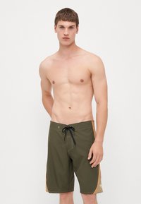 Olivgrüne Badeshorts mit kontrastierenden orangen Seitenakzenten, einem schwarzen Kordelzug und Steppnähten. Leichtes, synthetisches Material.