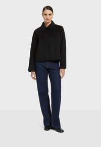 Čierna skrátená bunda s golierom, dlhými rukávmi a zapínaním na gombíky. Vydaná s tmavomodrými rovnými džínami a čiernymi topánkami.