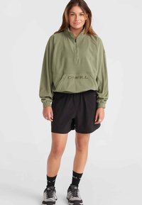 Olive green fleece pullover with a half-zip collar and front pocket. Paired with black shorts and gray hiking shoes, featuring black socks.