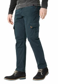 Dark teal cargo pants with multiple side pockets, a slim fit, and a brushed texture. Paired with black suede ankle boots and beige laces.