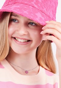 Roze handdoektextuur emmerhoed, gestreepte roze en crèmekleurige trui, zilveren ketting met een roze hart bedel, jeugdige glimlachende gezicht.